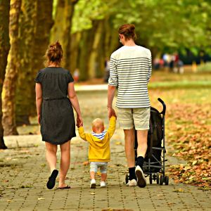 Familie mit Frau, Kleinkind und Mann von hinten fotografiert, spazierend entlang einer Allee im Herbst