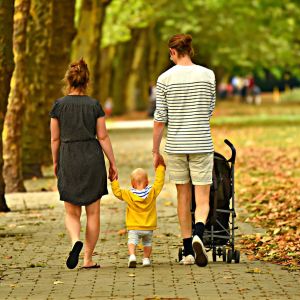 Familie mit Frau, Kleinkind und Mann von hinten fotografiert, spazierend entlang einer Allee im Herbst